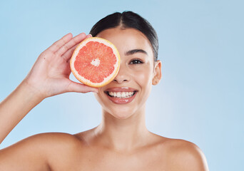 Fruit, beauty and skin of a woman with smile holding a grapefruit on her face against a blue studio background. Portrait of a happy female model in healthy, juicy and natural skincare for healthcare.