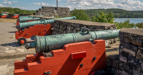 Row of 18th century bronze cannons with red base in firing position over Lake George with American flag