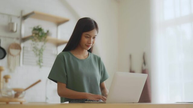 Smiling asian young woman working on laptop at home office. Young asian student using computer remote studying, virtual training, e-learning, watching online education webinar at house