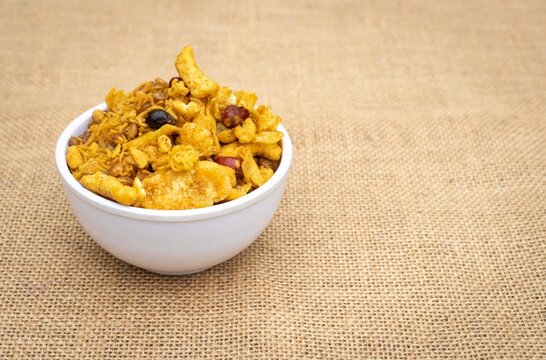 Spicy Chanachur in White Bowl Isolated on Burlap Fabric Background with Copy Space