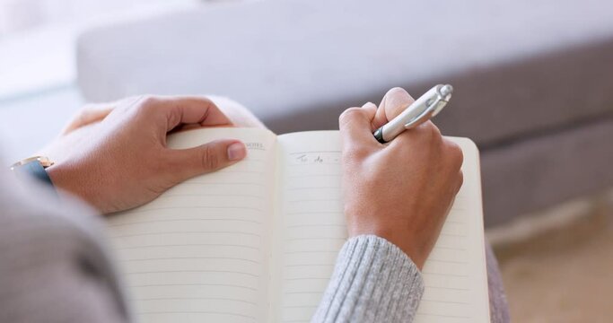 Woman hands writing in notebook, journal or diary with a pen and sitting on sofa while relaxing at home on the weekend. Female freelance writer relax and write a rough draft or sample in a book