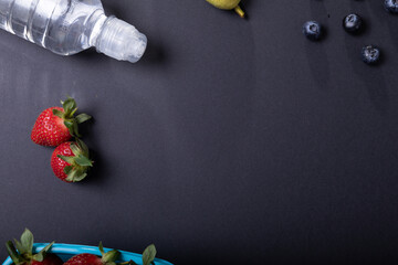 Overhead view of fruits with water bottle over black background, copy space
