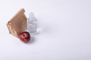 High angle view of paper lunch bag with apple and water bottle on white background along copy space