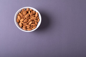 Overhead view of nutritious almonds in bowl over gray background with copy space