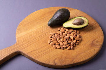 High angle close-up of avocado with almonds on wooden serving board against purple background