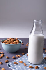 Close-up of milk bottle on napkin with almonds in bowl against gray background with copy space