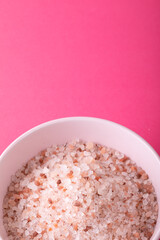 Close-up of himalayan rock salt in bowl on pink background with copy space