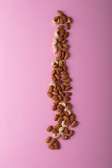 Overhead view of almonds and some cashews over pink background with copy space