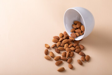 High angle view of almonds spilling from bowl on beige background with copy space