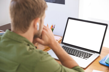 Man wearing wireless earphones looking at laptop at office