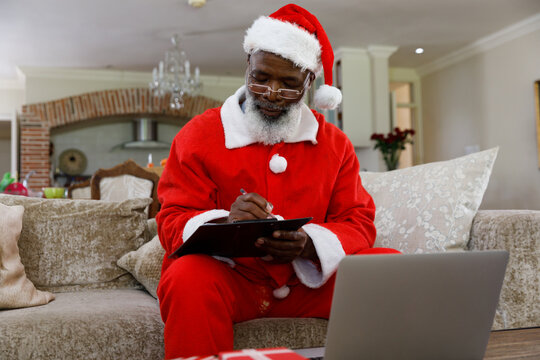 Senior African American Man Wearing A Costume Of Santa Claus And Writing On Clipboard