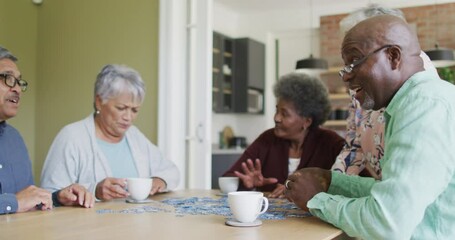 Group of happy diverse senior friends drinking coffee and doing puzzle at home