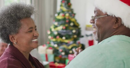 Happy african american senior couple dancing together with friends in background at christmas time - Powered by Adobe
