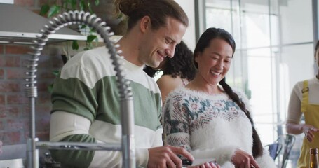 Happy group of diverse female and male friends cooking together in kitchen