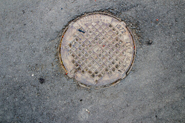 Old iron metal manhole cover sewer cap on the city street asphalt