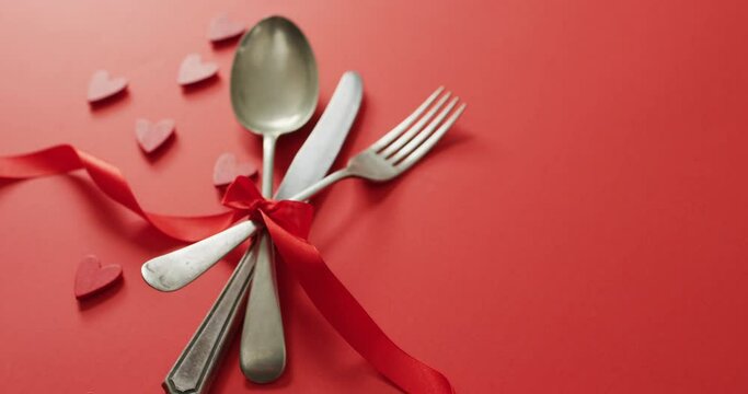 Red ribbon and cutlery with hearts on red background at valentine's day