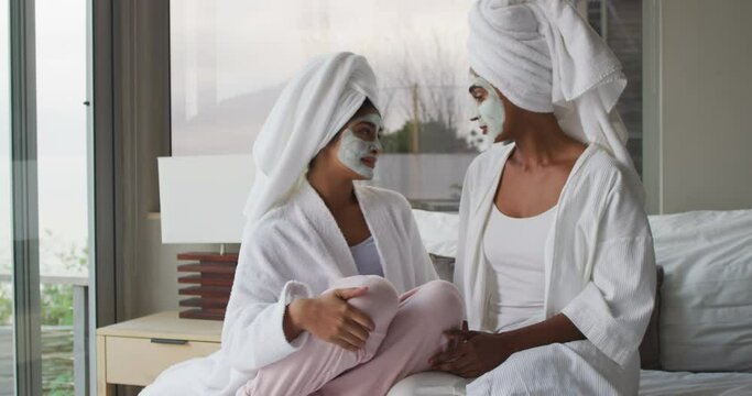 Video of relaxed diverse female friends moisturizing with face masks and talking in bathroom