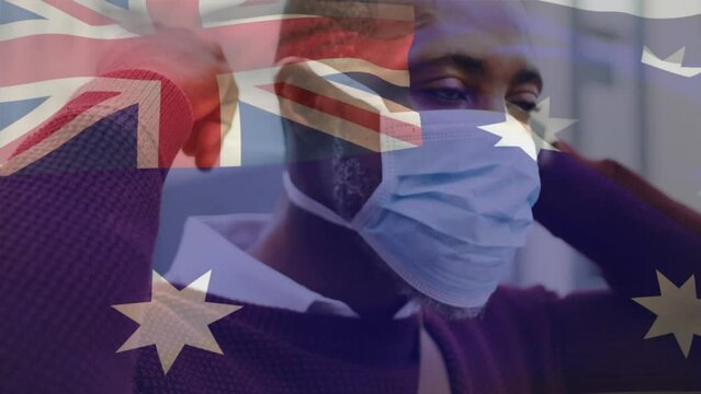 Animation of flag of australia waving over african american man wearing face mask in city street