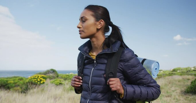 Mixed race woman wearing backpack looking at camera hiking in countryside