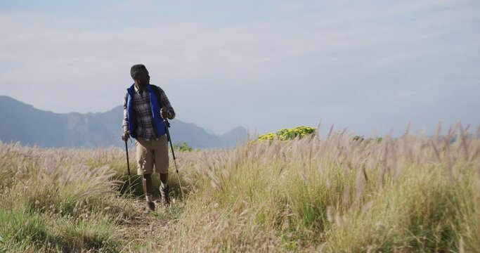 African american man wearing backpack using nordic walking poles hiking in countryside