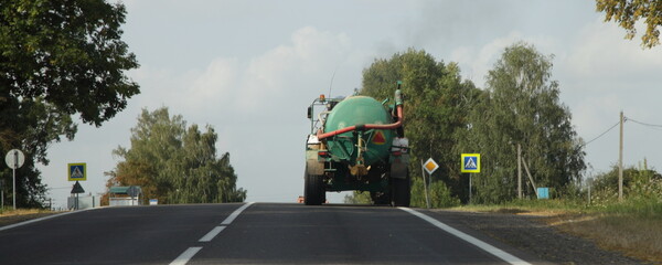 Green sewerage truck drive on country road at summer day. Sewage disposal service on countryside