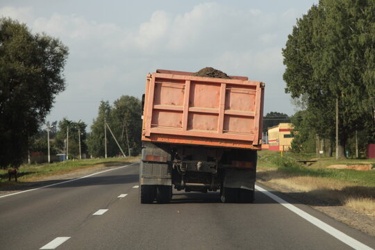 Heavy overloaded curvy dumper truck drive with bulk cargo on a European countryside asphalt road at summer day