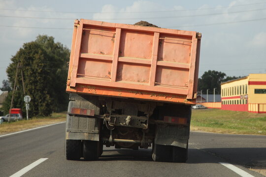 Heavy overloaded dump truck with lurch carries sand on a European countryside asphalt road at summer day