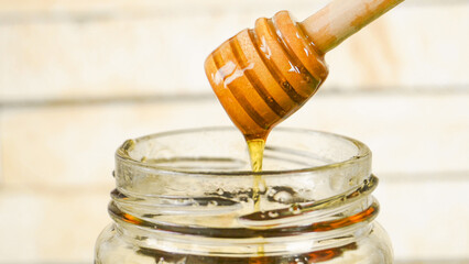 Honey dripping from a honey dipper into a glass honey jar with wood background.