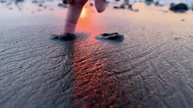 Clos-up view of finger drawing a smile emoji on wet sand at sunset. Happy vacation dusk scene on a beach. Film grain. Soft focus. Live camera. Blur