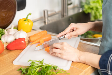 Asian young woman, girl or housewife hand using knife, cutting carrots on  board, on wooden table in kitchen home, preparing ingredient, recipe fresh vegetables for cooking meal. Healthy food people.