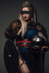 Fototapeta na wymiar Shot of medieval female hunter with fur holding shield and helmet against gray background.