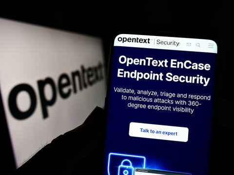 Stuttgart, Germany - 08-27-2022: Person holding cellphone with webpage of Canadian software company OpenText Corporation on screen with logo. Focus on center of phone display.