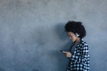 Mixed race woman against grey wall using smartphone with headphones on