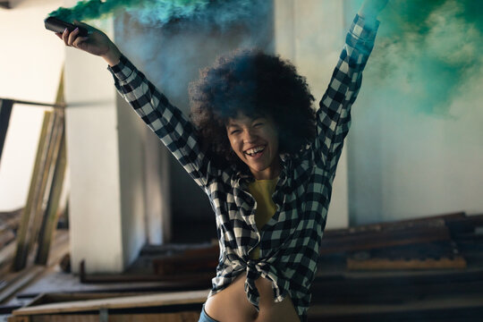 Mixed race woman in an empty building holding up a green flare laughing