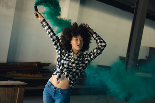 Mixed race woman in an empty building holding up a green flare - Powered by Adobe