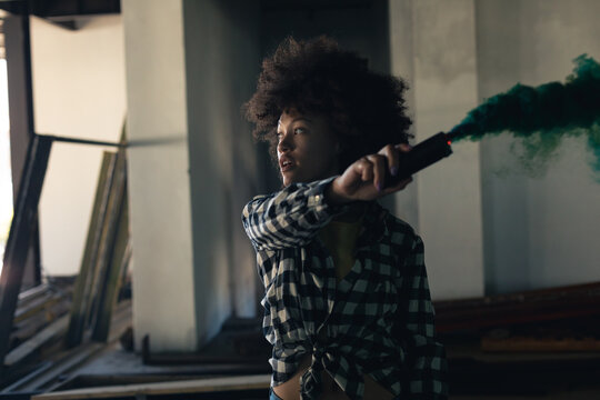 Mixed race woman in an empty building holding a green flare - Powered by Adobe