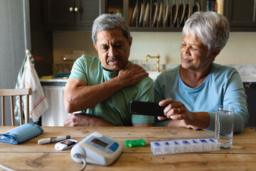Senior african american couple sitting by table using smartphone