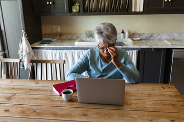 Senior african american woman sitting by table using laptop drinking coffee