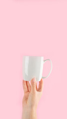 Arms raised up holding coffee cup on pink background.