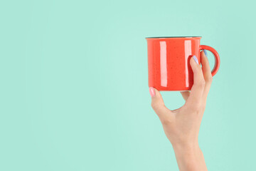 Arms raised up holding tea cup on green background.