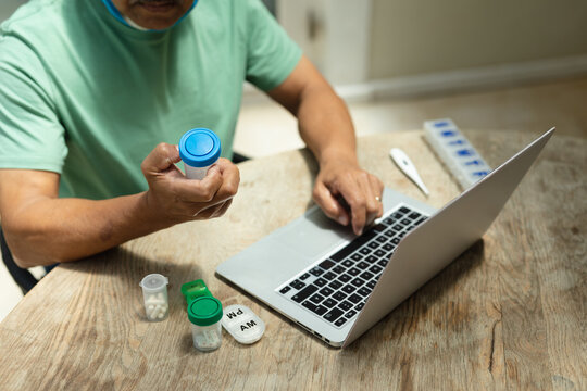 Senior African American Man Wearing Mask Holding Medicine Using Laptop