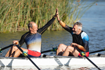 Two senior caucasian male rowers high fiving each other while rowing the boat on the lake