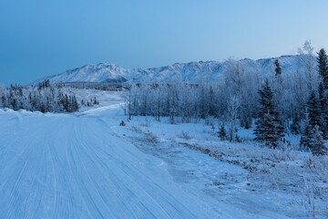 Fototapeta na wymiar Chugach mountains in frosty winter twilight. Alaskan snow-covered forest road through the snow-covered taiga 