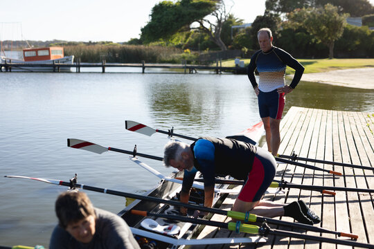 Senior caucasian rowing team attaching oars to the boat near the wooden dock