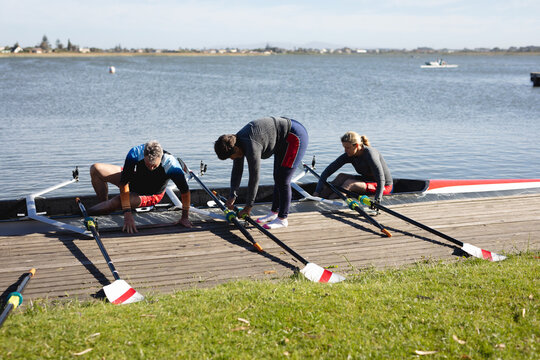 Senior caucasian rowing team attaching oars to the boat near the wooden dock