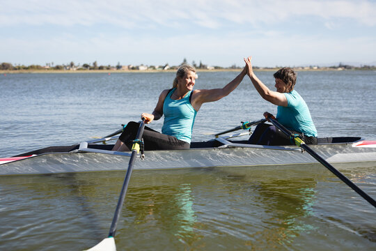 Two senior caucasian female rowers high fiving each other while rowing the boat on the lake