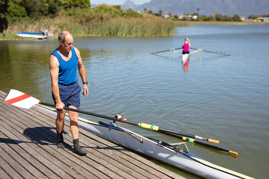 Senior caucasian male rower keeping boat oars in the boat while standing on the wooden dock