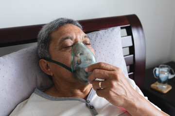 Senior mixed race man lying in bed at home using a face mask ventilator