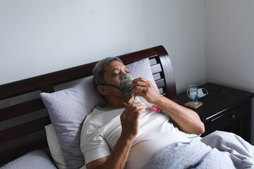 Senior mixed race man lying in bed at home using a face mask ventilator