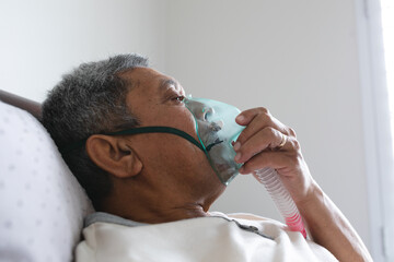 Senior mixed race man lying in bed at home using a face mask ventilator